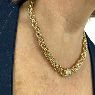 Gold chain necklace worn by a person with a blue garment in the background