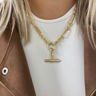 Gold chain necklace with a clasp on a person wearing a white shirt and brown jacket.