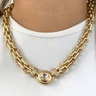 Gold chain necklace with a central gemstone on a white background
