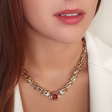 Close-up of a gold chain necklace with a red gemstone pendant worn by a person.