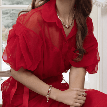 Person wearing a red dress with ruffled sleeves and gold jewelry indoors.