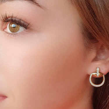 Close-up of a woman wearing a gold hoop earring with a pink top.