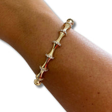A gold bamboo-style bangle bracelet with small clear pavé accents, shown worn on a person's wrist against a plain white background.