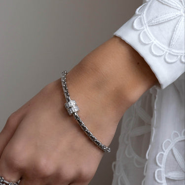 Hand wearing a silver bracelet and ring on a neutral background