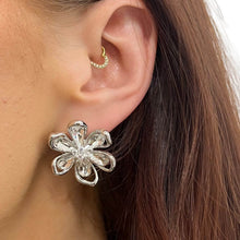 A close-up of a person's ear wearing a silver flower-shaped stud earring and a small gold hoop in the cartilage.