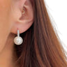 A close-up of a woman's ear wearing a dangling pearl earring with a silver pavé top and a small gold hoop earring in the opposite ear.