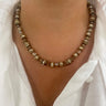 A close-up of a person wearing a beaded necklace made of faceted brown and cream beads with metallic gold-toned spacer details, styled with a white collared shirt.