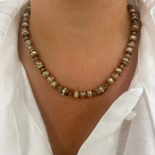 A close-up of a person wearing a beaded necklace made of faceted brown and cream beads with metallic gold-toned spacer details, styled with a white collared shirt.