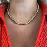 A close-up of a person's neck and upper chest wearing a two-tone gold and silver curved necklace over a bright coral-red knit top.
