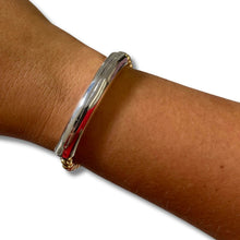 A polished silver-toned metal bangle bracelet with a small gold-toned accent at the bottom, shown worn on a person's wrist against a plain white background.