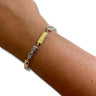 A gold and silver bracelet worn on a person's wrist, featuring a central polished gold bar, textured silver links, and a small red gemstone accent.