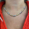 A close-up of a person's neck and chest wearing a gold and silver beaded necklace over a bright orange knit top.