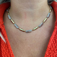 A close-up of a person's neck and chest wearing a gold and silver beaded necklace over a bright orange knit top.