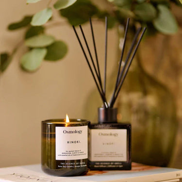 Osmology Hinoki candle and diffuser on a surface with greenery in the background