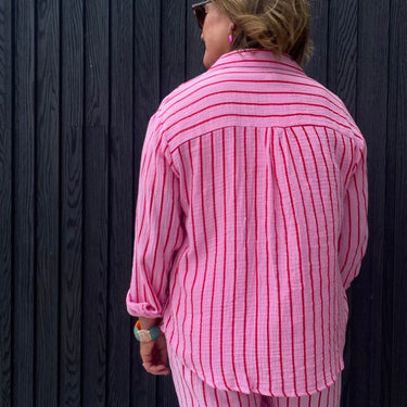Person wearing a pink striped shirt against a dark wooden wall