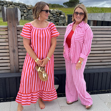 Two women in matching pink and white striped outfits standing outdoors near a stone wall.