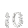 A pair of silver huggie hoop earrings adorned with clear round-cut and baguette-cut gemstones, shown on a solid white background.