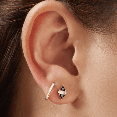 Close-up of an ear wearing a diamond hoop earring and a black and gold stud earring.