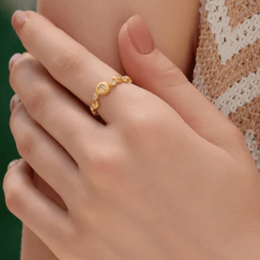 Close-up of a hand wearing a gold ring with a green background