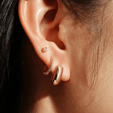 Close-up of an ear wearing gold hoop earrings with a blurred background