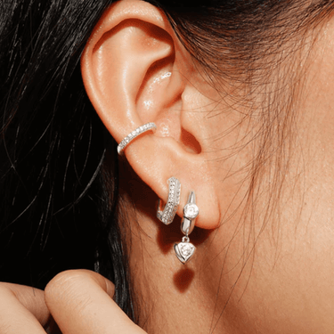Close-up of an ear wearing silver hoop earrings with heart-shaped gemstones.