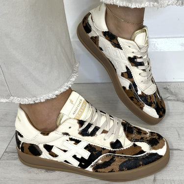 Leopard print sneakers worn with light-colored pants on a wooden floor.