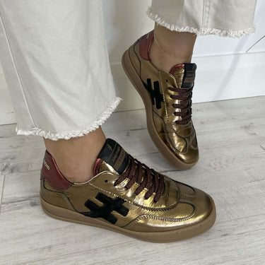 Gold sneakers with maroon accents worn on a light wooden floor.