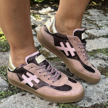 A person wearing pink and black patterned sneakers with gum soles, standing on a stone path outdoors.