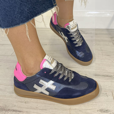 Navy blue sneakers with gum toned soles worn indoors on a wooden floor.