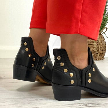 Black boots with gold buttons worn with red pants on a light wooden floor.