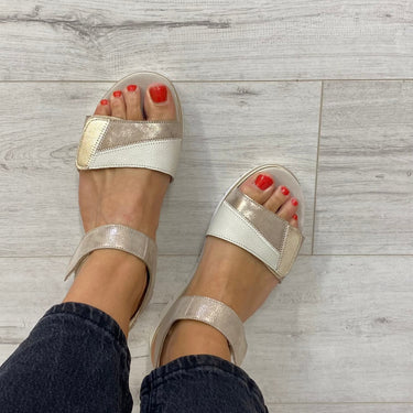 White sandals with clear straps worn on a light wooden floor.