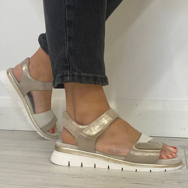 Beige sandals worn with black pants on a light wooden floor.