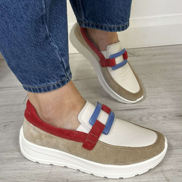 Beige and white sneakers with red and blue straps worn with blue jeans on a wooden floor.