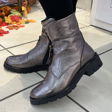 A pair of metallic taupe leather ankle boots with black soles and side zippers, worn with black tights on a tiled floor.