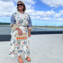 Woman in a floral dress with a colorful bag standing on a rooftop with a scenic view.