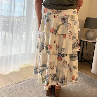 Person wearing a floral tiered skirt in a room with a lamp and window.