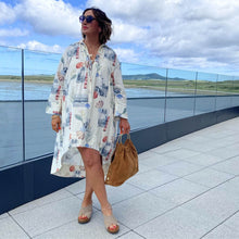 Woman in a floral dress standing on a rooftop with a scenic view of water and mountains.