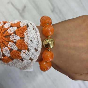 Hand wearing an orange beaded bracelet with a gold accent on a white marble surface.