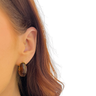 Close-up of an ear wearing a gold hoop earring with a plain background