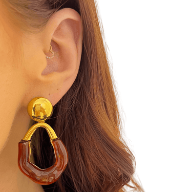 Gold and amber earring worn by a person with a plain background