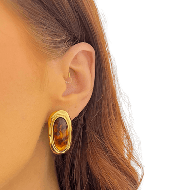 Gold earring with amber stone worn by a person with brown hair on a white background
