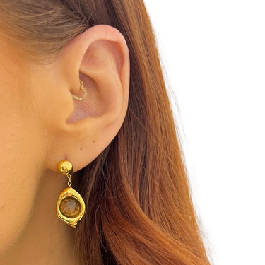 Close-up of a person wearing a gold earring with a gemstone on a white background