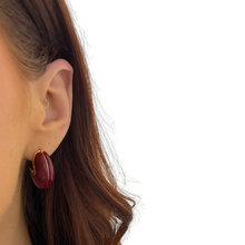 Close-up of a person wearing a burgundy hoop earring on a white background