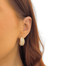 Close-up of an ear wearing a gold and beige earring with a blurred background