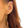 Gold earring with a tiger's eye stone worn by a person with long brown hair.
