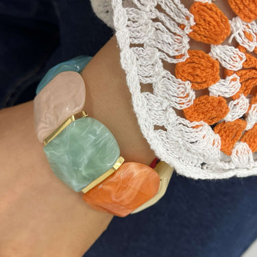 Close-up of a colorful bracelet on a person wearing a white lace garment with orange patterns.