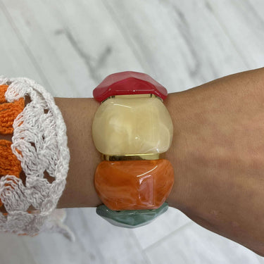 Close-up of a wrist wearing a bracelet with colorful beads on a light wooden surface.
