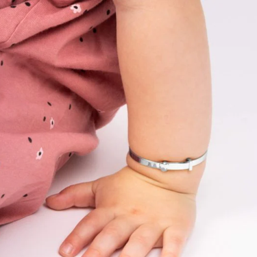 Child wearing a pink outfit with a pattern and a silver bracelet on a white background