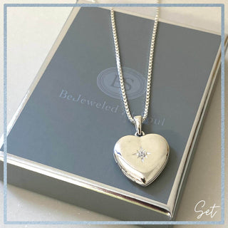 Silver heart-shaped locket with a diamond on a gray surface with 'BeJeweled' branding.