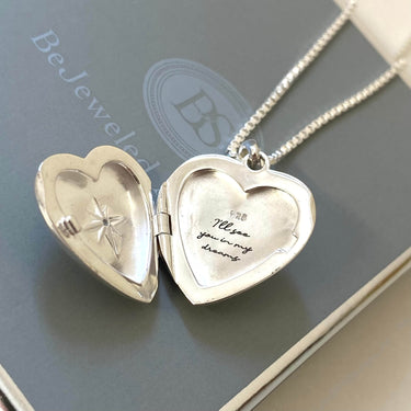 Silver heart-shaped locket with engraved text on a gray surface, branded 'BeJeweled'.